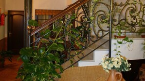 A staircase with ornate metal railings, a wicker chair, a round wooden table with a vase of flowers, and a potted plant. - Hotel Rural El Olivo (La Puebla de los Infantes)