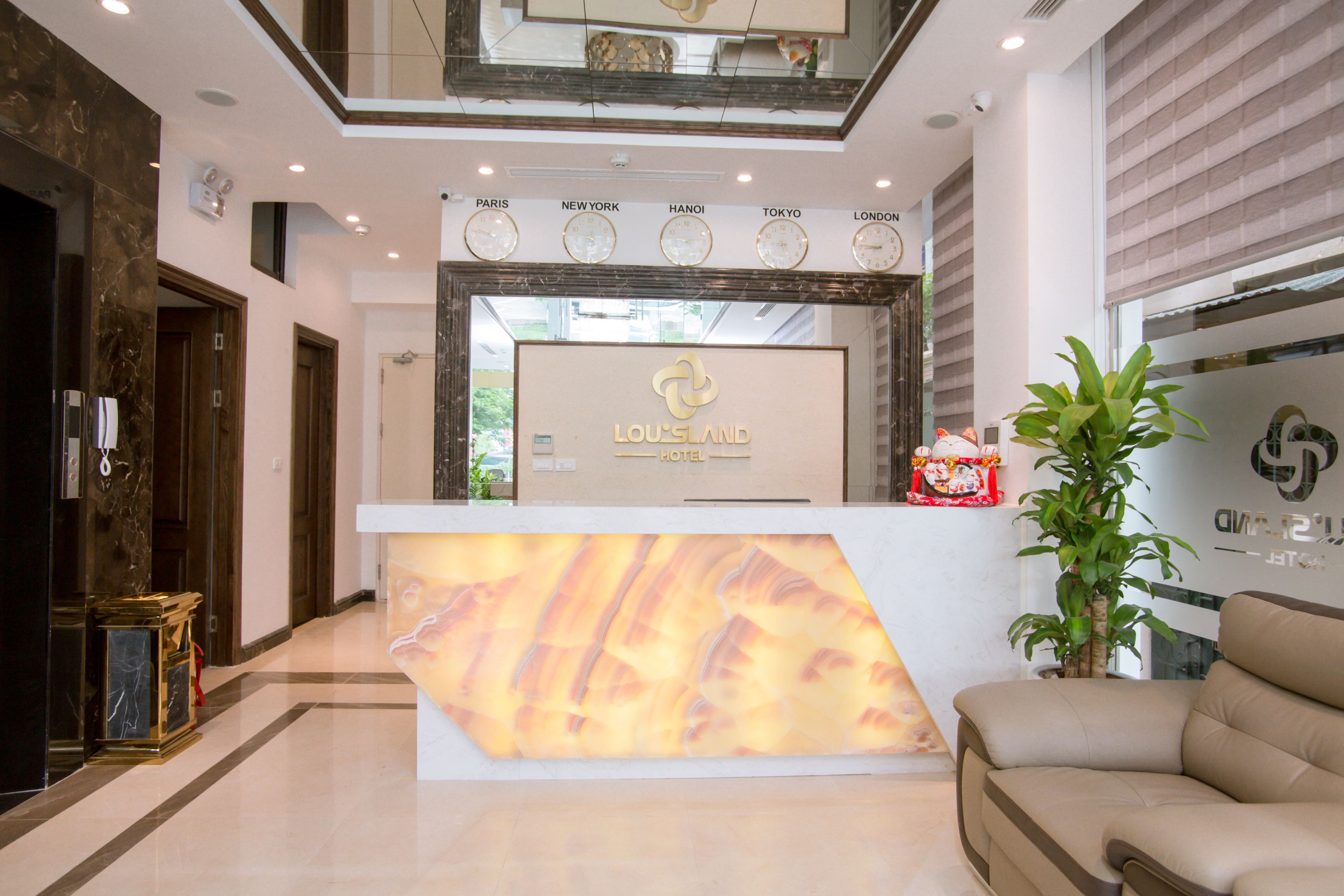 A hotel reception area with a modern design, featuring a reception desk, a seating area, and a decorative wall with clocks indicating different cities.