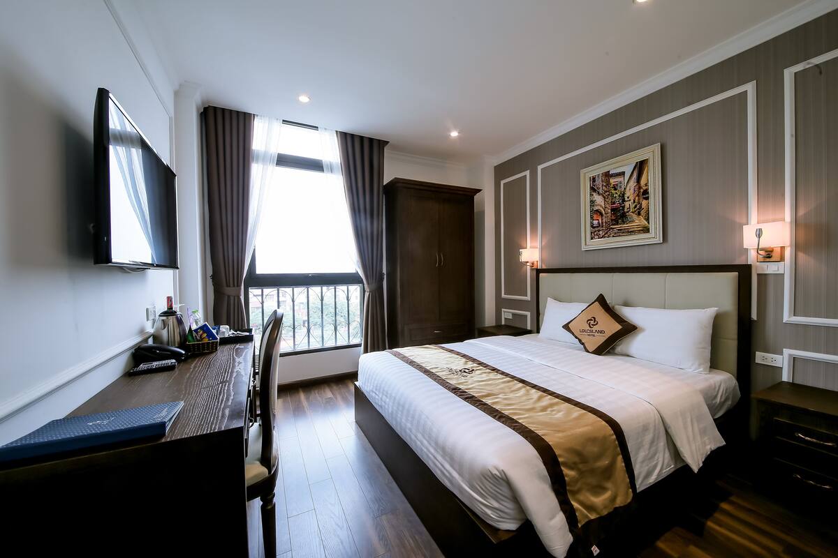 A hotel room with a bed, desk, chair, TV, and a window with curtains.