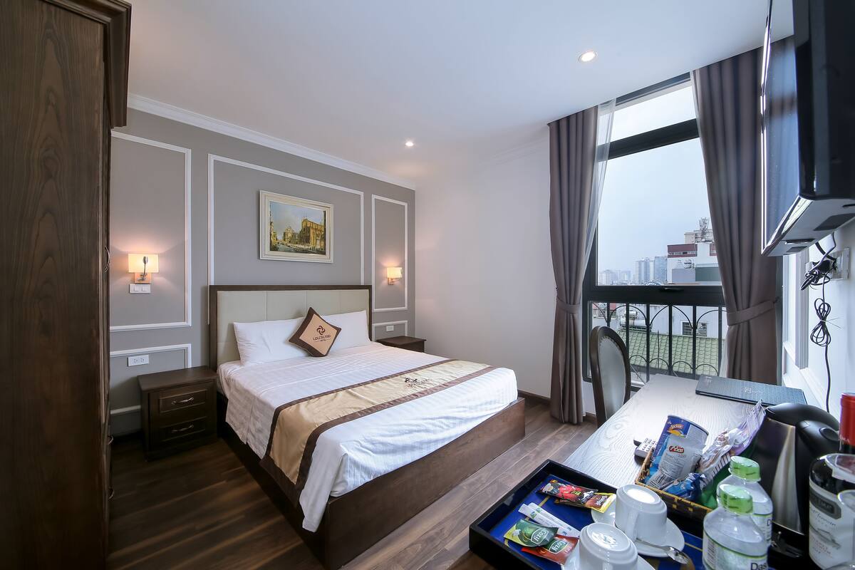 A hotel room with a large bed, bedside lamps, a table with breakfast items, and a city view.