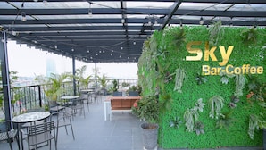 A rooftop bar with a green wall, tables, chairs, and a view of the city. - Louisland Hotel (Hanoi)