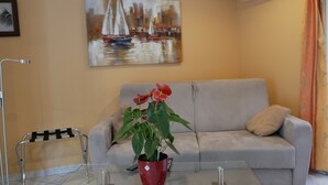 A living room with a sofa, a glass coffee table, a red potted plant, a painting on the wall, and a chair. - Villa Seignemartin (Lyon)