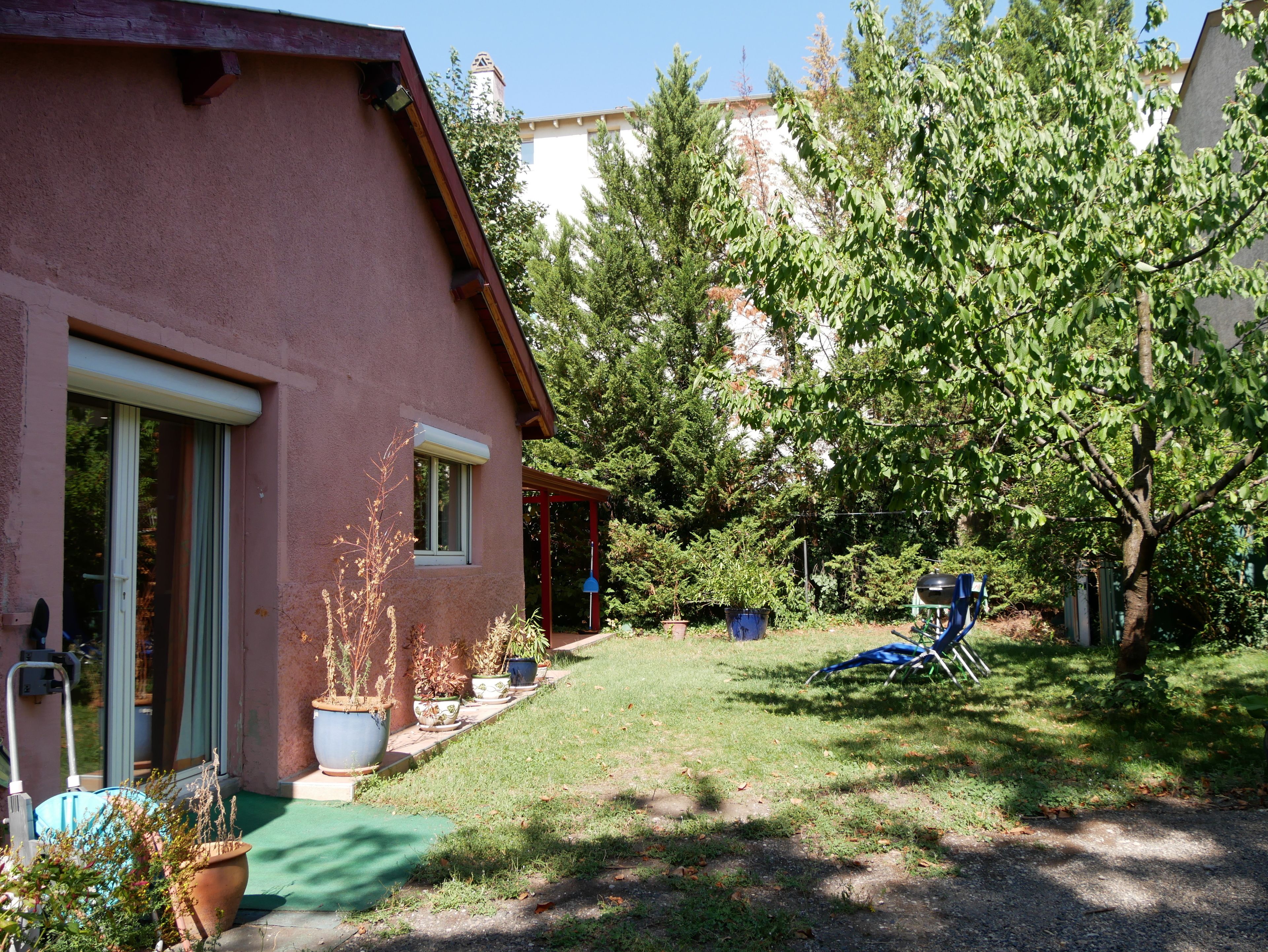 Una casa con fachada roja, un porche cubierto y un jardín.