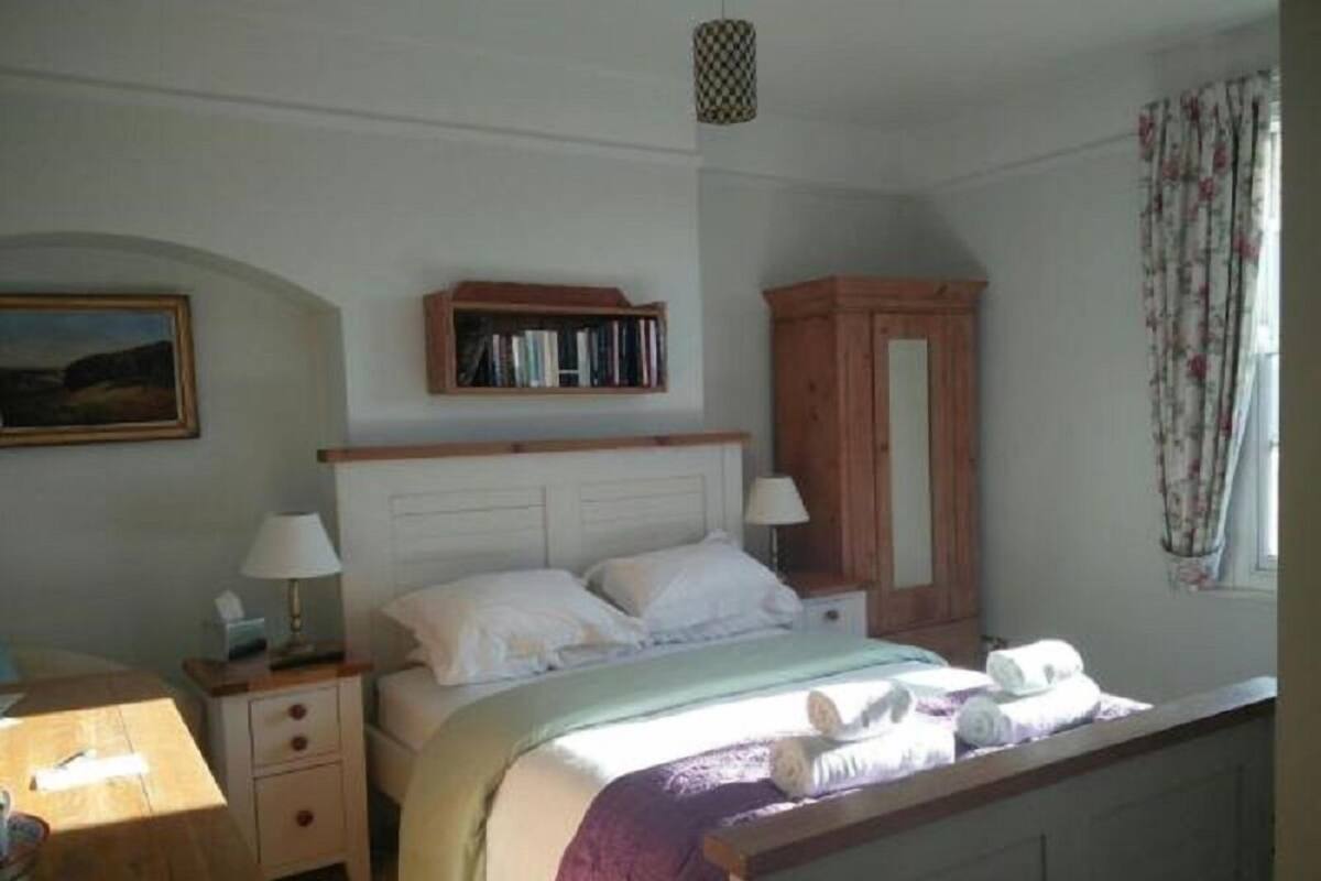 A bedroom with a bed, nightstands, a wooden wardrobe, a bookshelf, and a window with curtains.