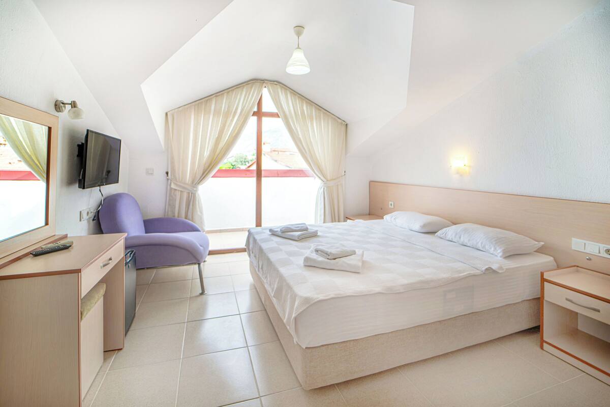 A hotel room with a bed, a desk, a chair, a TV, and a window with curtains.