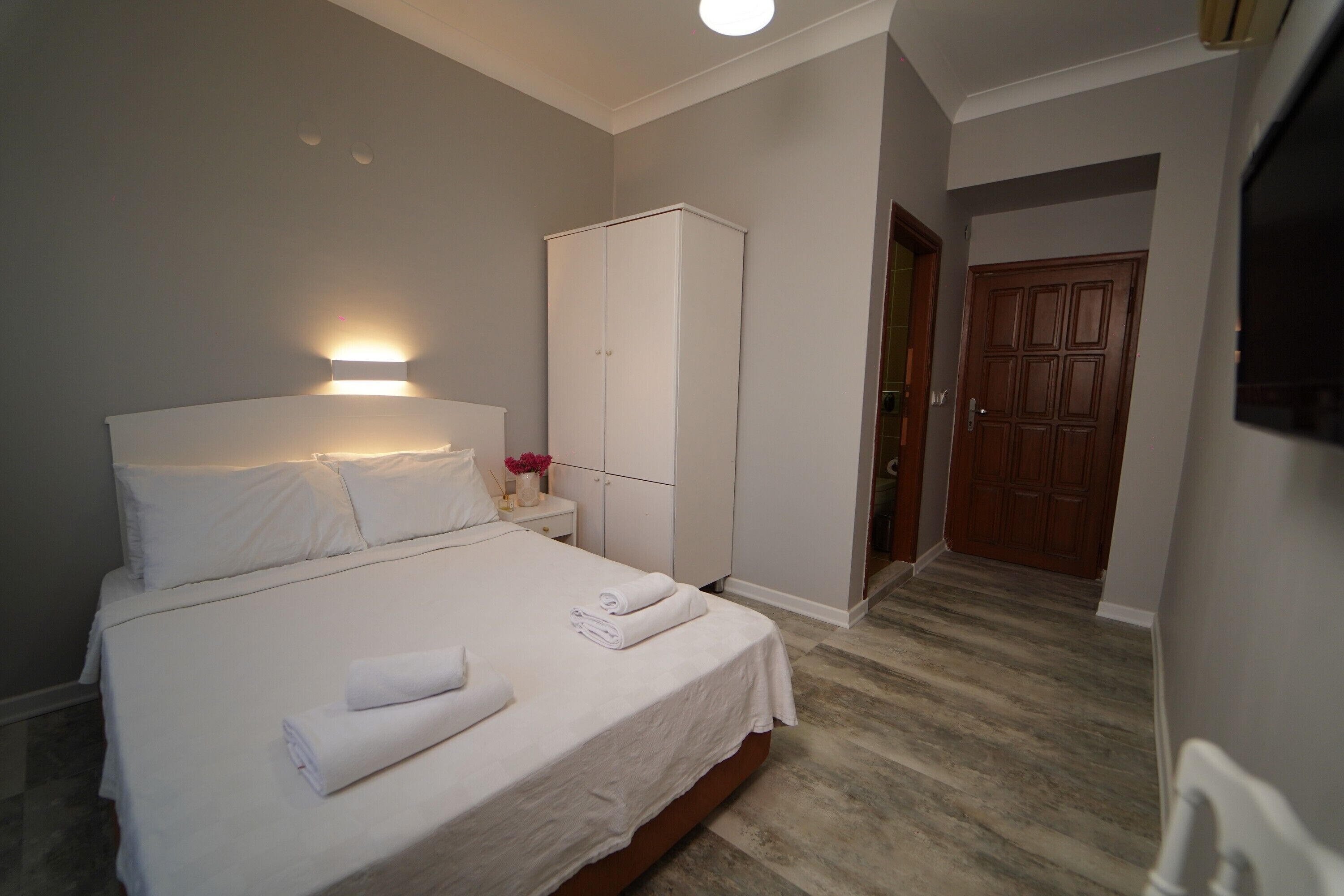Un lit bien fait, avec du linge de lit et des serviettes blanches, une armoire blanche et une porte en bois, dans une chambre d’hôtel.