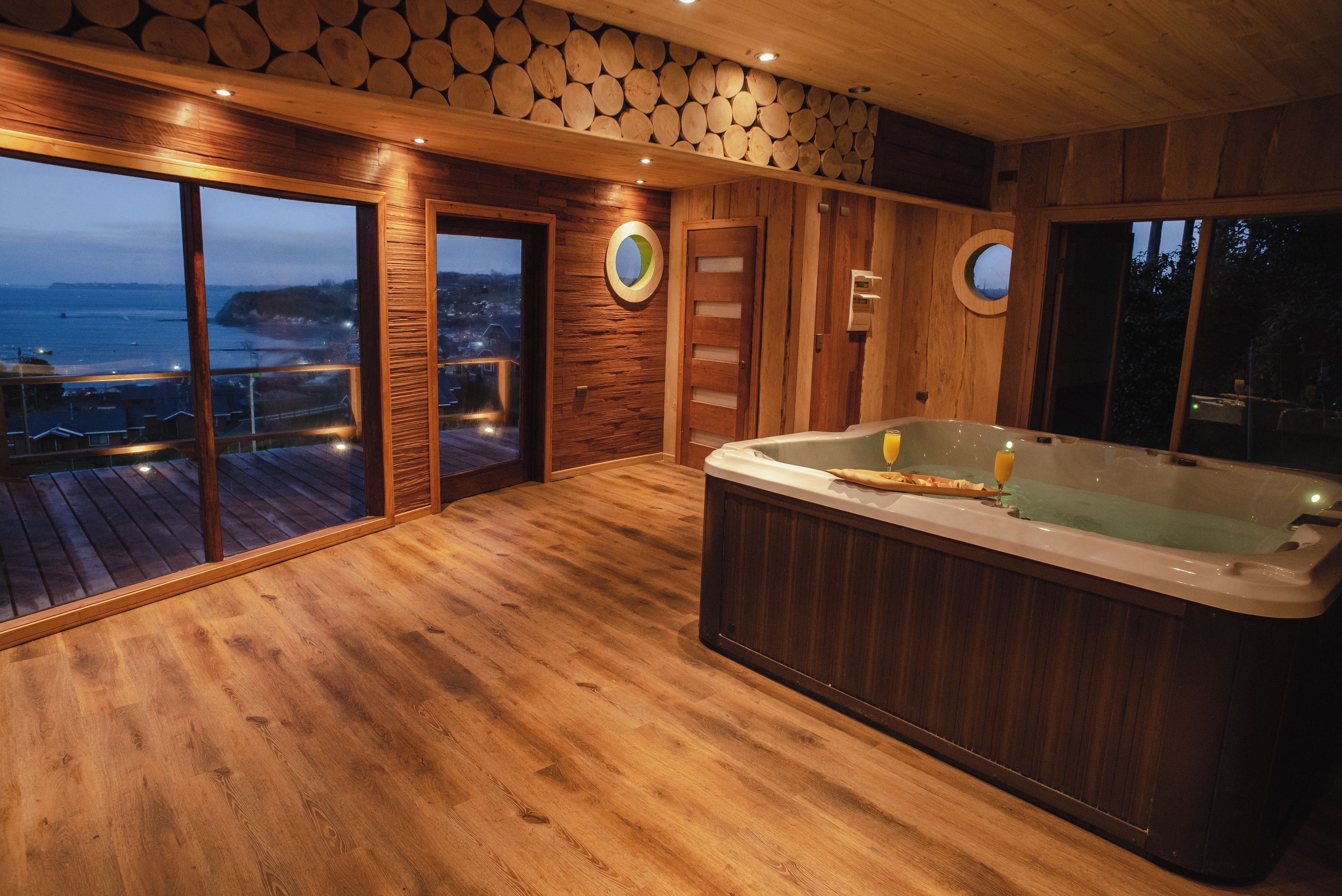 Un interior de madera con un jacuzzi, ventanas amplias y vista al mar.