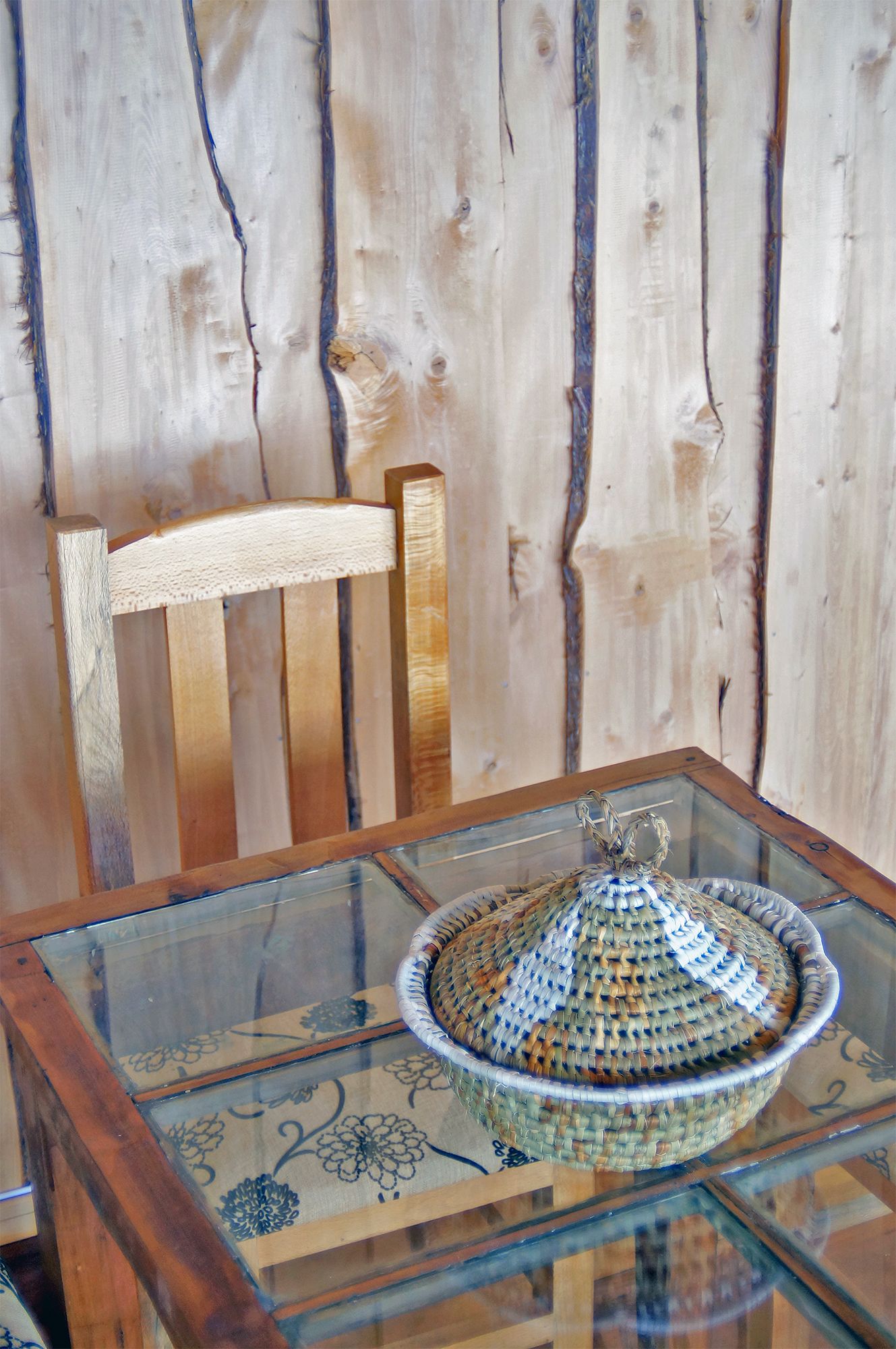 Una silla de madera y una mesa de vidrio con una cesta tejida.
