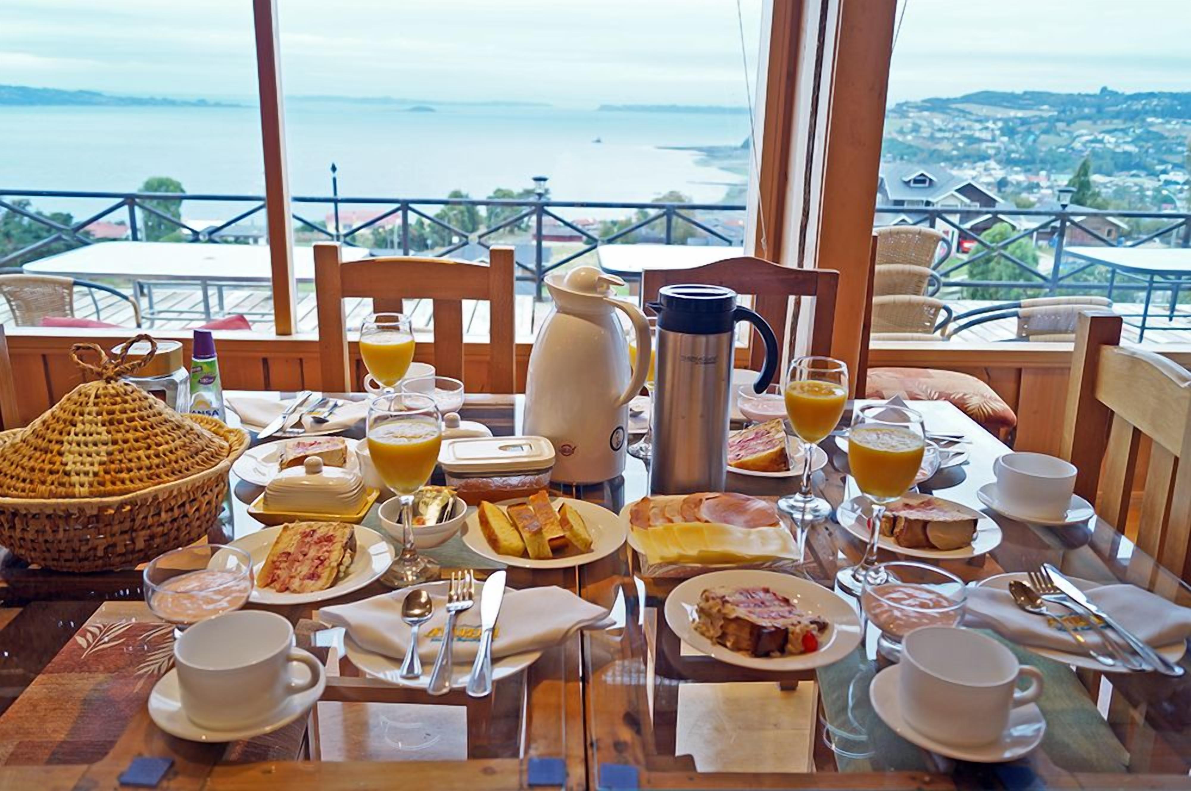 Una mesa de desayuno preparada con diferentes platos, una cafetera y vistas a un paisaje costero.