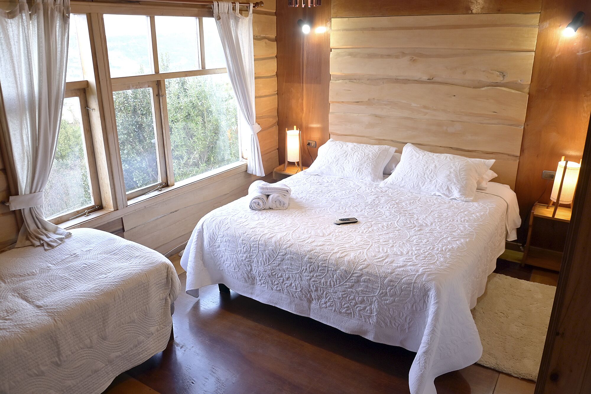 A bedroom with a large bed, two bedside tables, a chair, and a window with curtains.