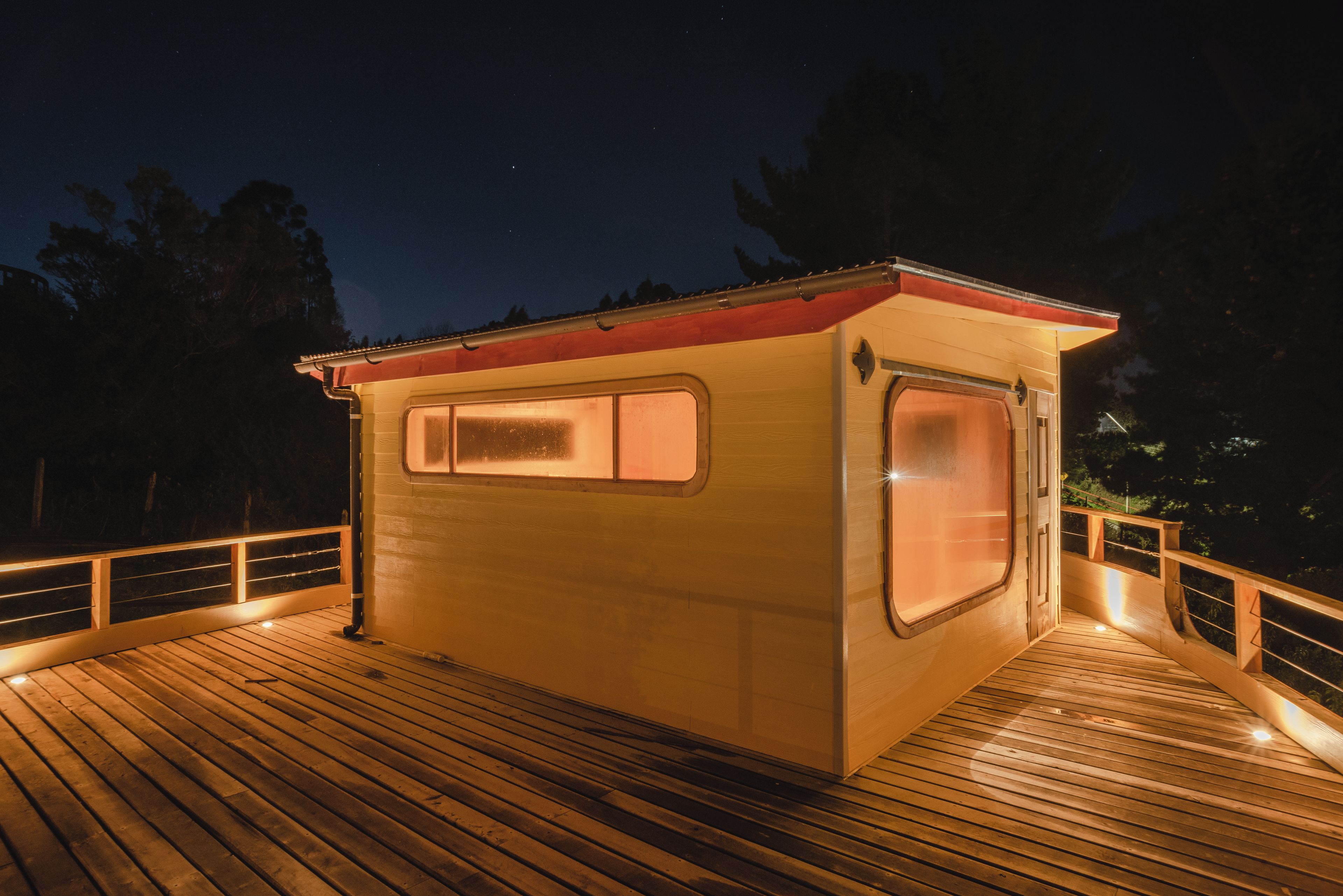 Eine kleine, einräumige Hütte mit Fenster und Tür, auf einer Holzterrasse mit Geländern gelegen.