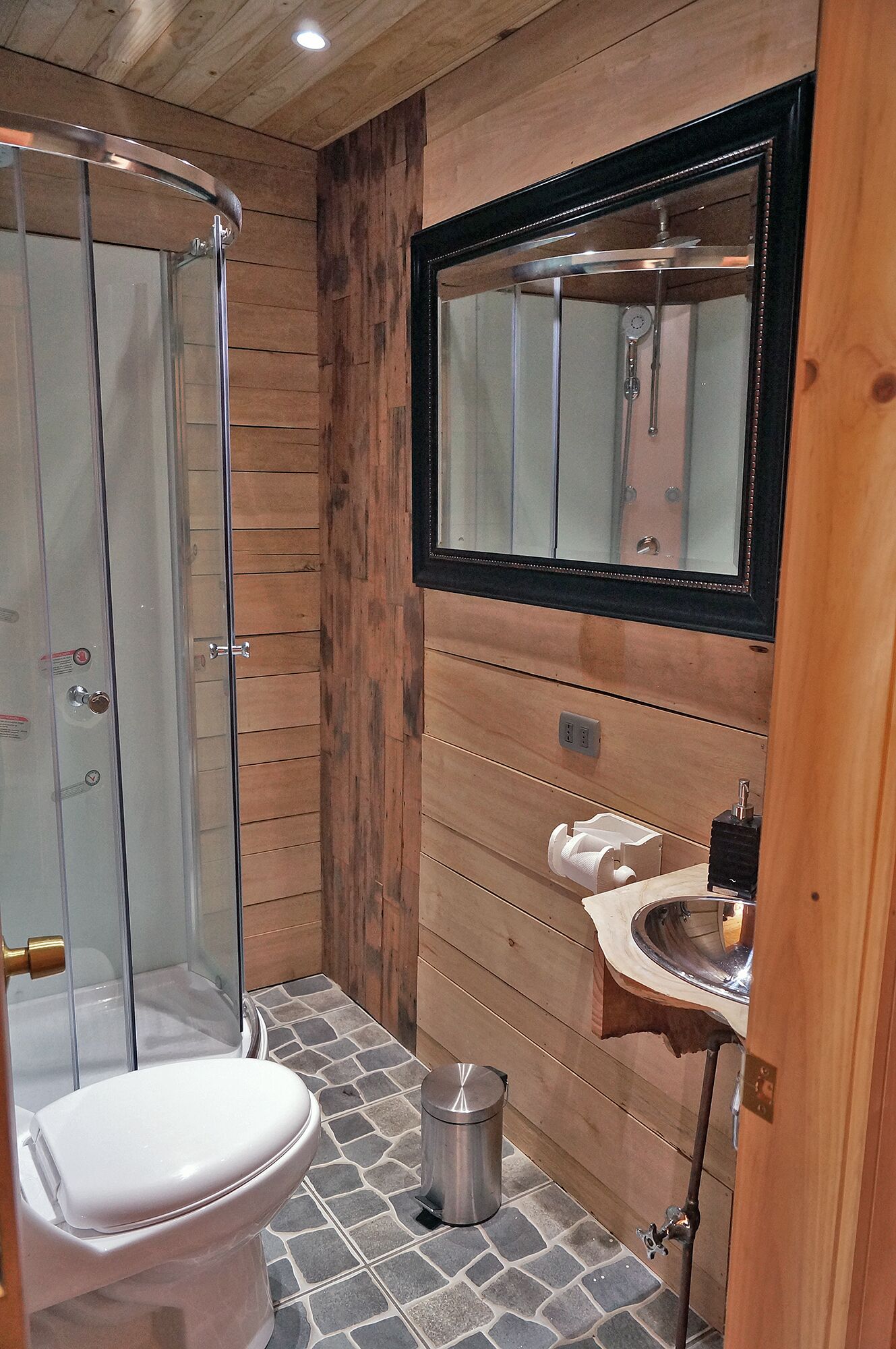 Une salle de bain avec une douche à parois de verre, des toilettes blanches, un lavabo avec un miroir au-dessus et une poubelle.