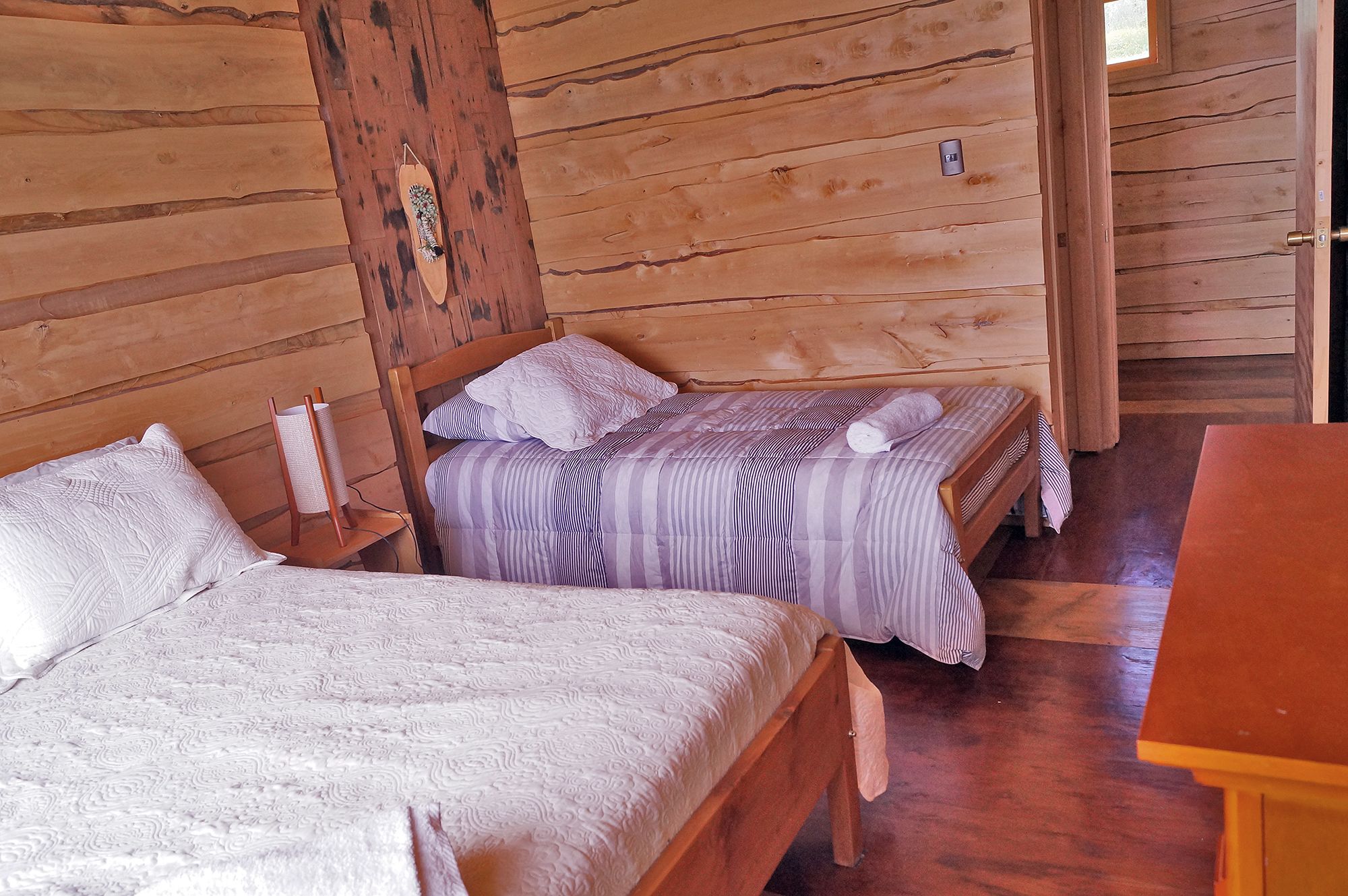 Quarto tipo cabana de madeira com duas camas, cada uma com manta e almofadas listradas.