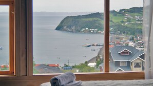 Un dormitorio con un ventanal que da a una ciudad costera, una cama y vistas de barcos en el agua.