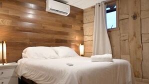 Un dormitorio con cabecera de madera, una cama blanca, una mesita de noche, una lámpara y una ventana con cortina.