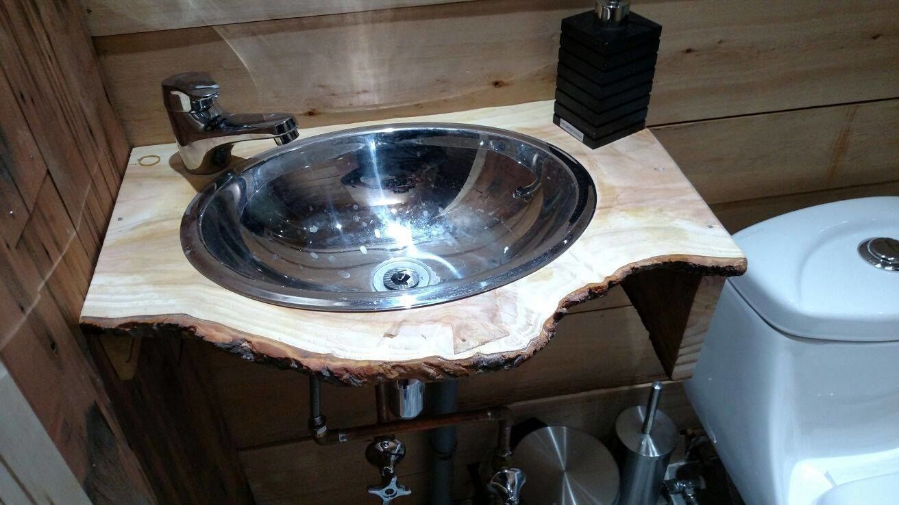 Un baño con tocador de madera, lavamanos de acero inoxidable y váter blanco.