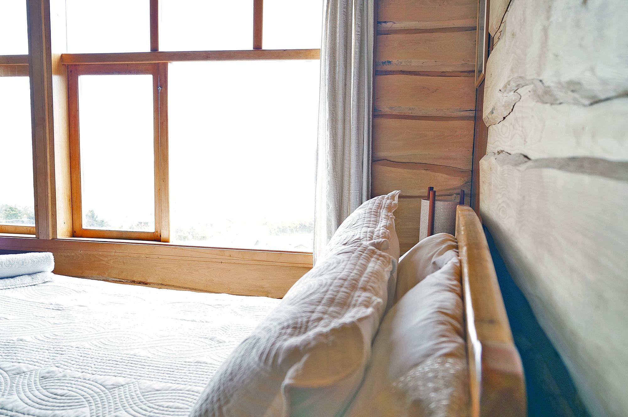 A bedroom with a wooden headboard, a window with curtains, and a patterned rug on the floor.
