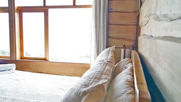 A bedroom with a wooden headboard, a window with curtains, and a patterned rug on the floor.