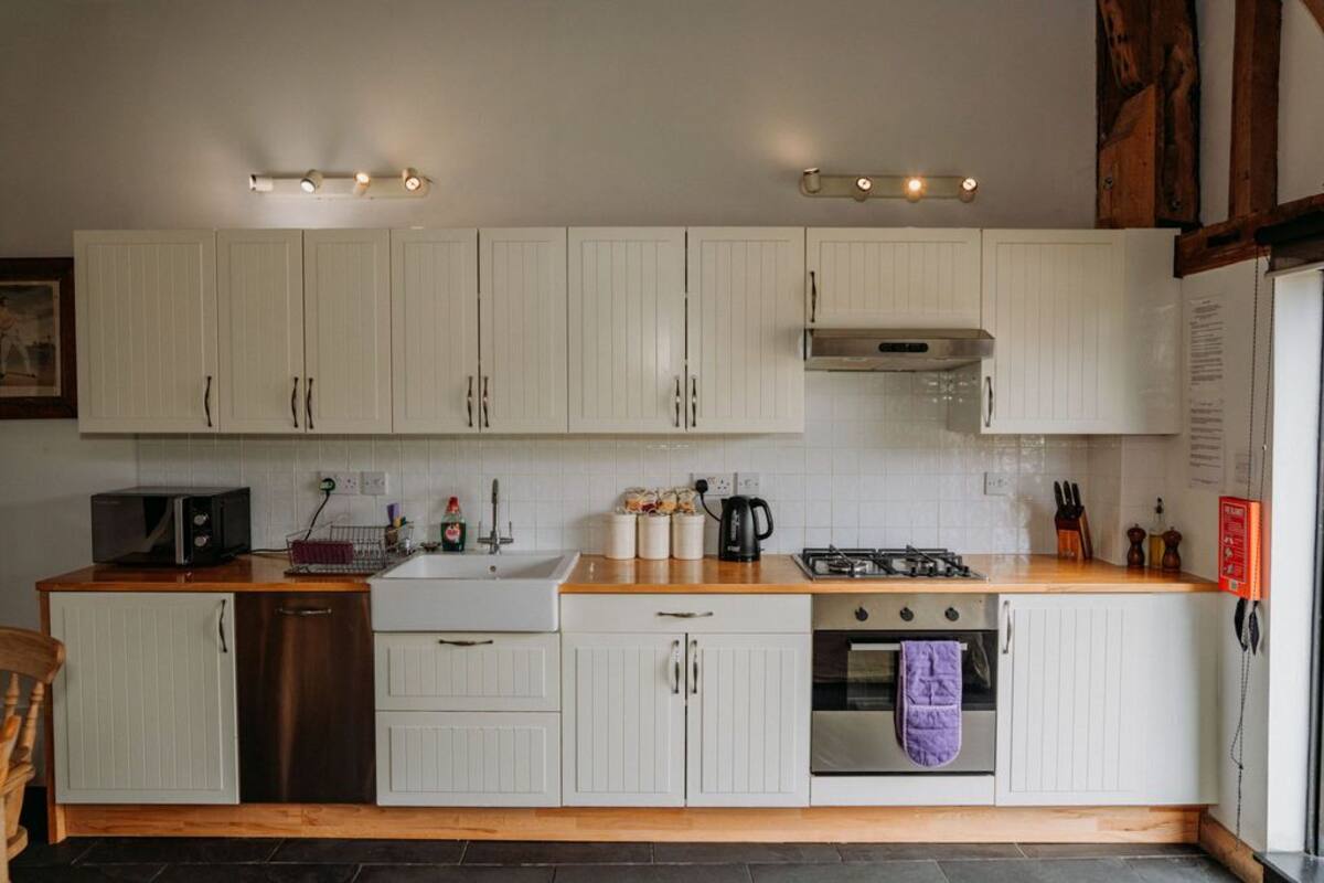 A kitchen with white cabinets, a wooden countertop, a microwave, a sink, a stove, and a hanging oven mitt.
