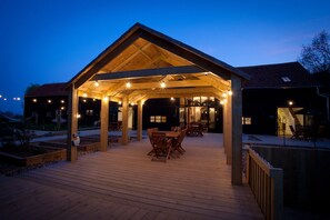 Un patio techado al aire libre con mobiliario de madera y luces colgantes.