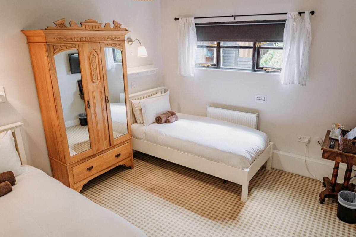 A bedroom with a wooden wardrobe, a single bed, a window with curtains, and a radiator.