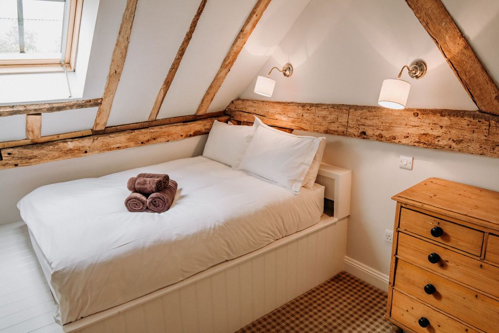 A bedroom with a wooden ceiling, a bed with white linens, two bedside lamps, and a wooden dresser.