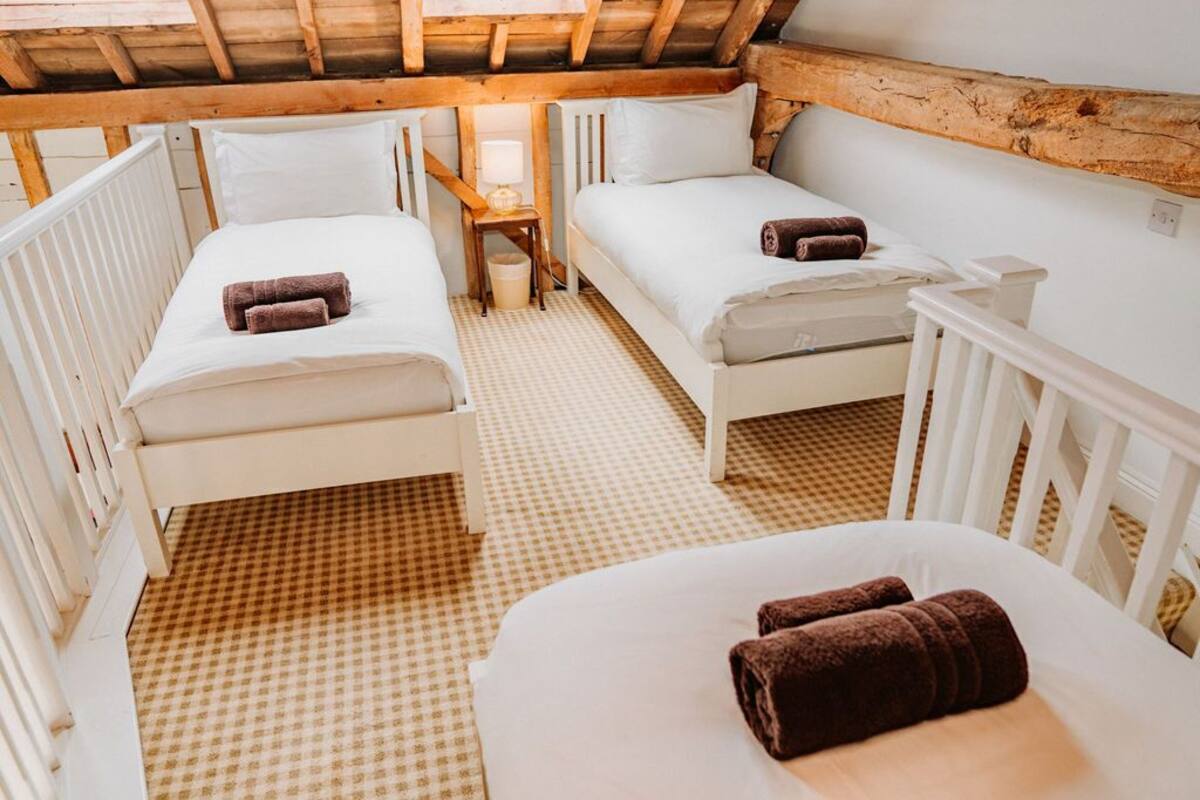 A cozy attic bedroom with two single beds, a small table with a lamp, and a checkered floor.
