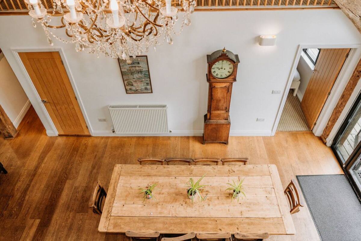 A dining area with a wooden table, chairs, potted plants, a chandelier, a wall clock, and a radiator.