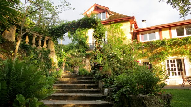 Eine Steintreppe führt zu einem Haus, das von üppigem Grün und Efeu umrankt ist.