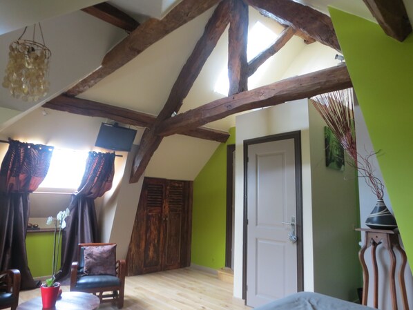 A room with exposed wooden beams, a green wall, a door, and a window with curtains.