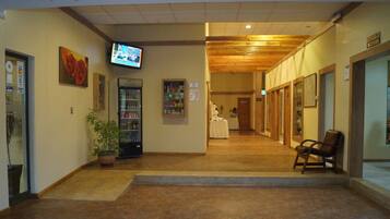 A hotel lobby with a reception desk, a television screen, a vending machine, and a potted plant.