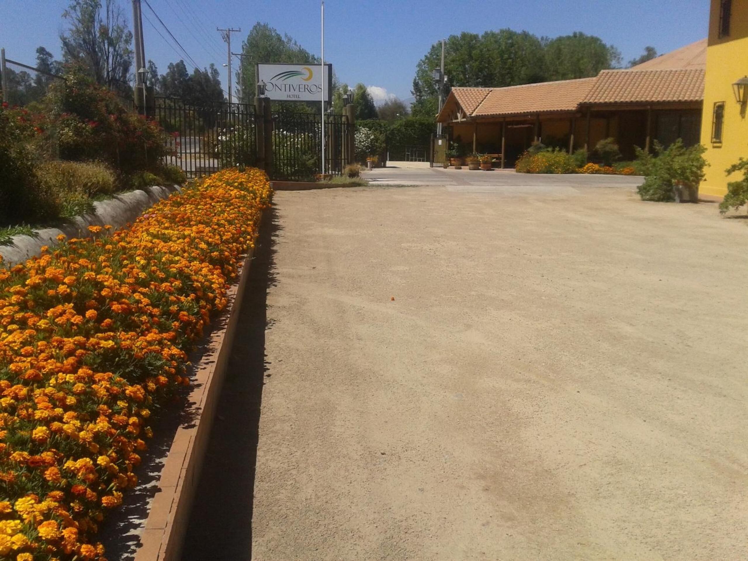 L’entrée d’un hôtel, avec un panneau indicateur, une allée pavée et un parterre fleuri aux fleurs orange.