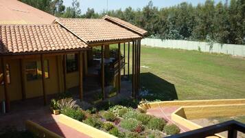 Een geel gebouw met een pannendak, een overdekte patio en een goed onderhouden tuin met verschillende planten en bloemen.