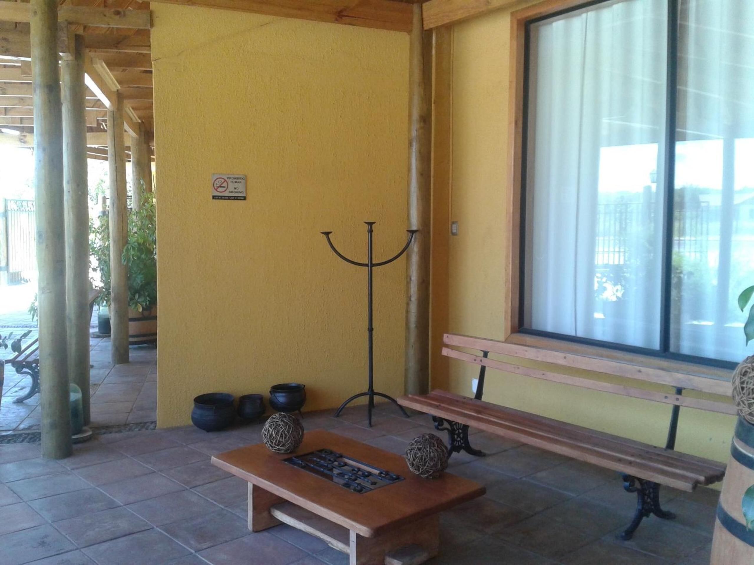 A covered outdoor area with a wooden bench, a table with decorative items, and a wall-mounted sign.
