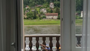 Habitación con balcón que da a un lago, una silla y vistas a casas y vegetación.