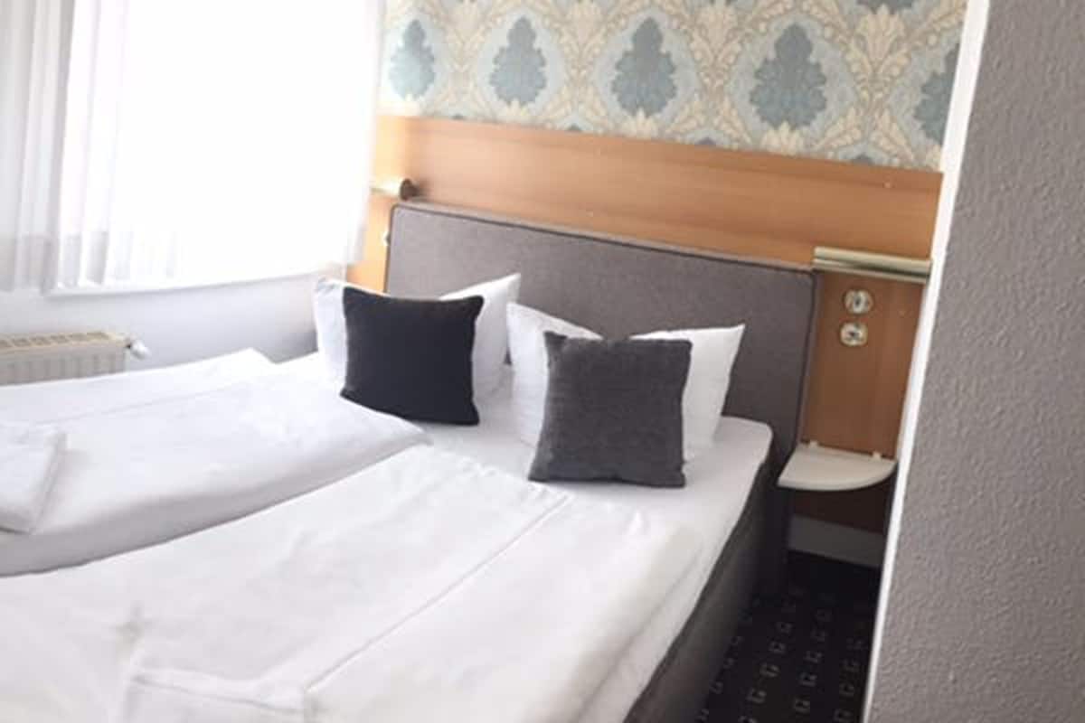 Ein Hotelzimmer mit Doppelbett, zwei Kissen, einem Holz-Kopfteil, einem Nachttisch und einer Wand mit Muster.