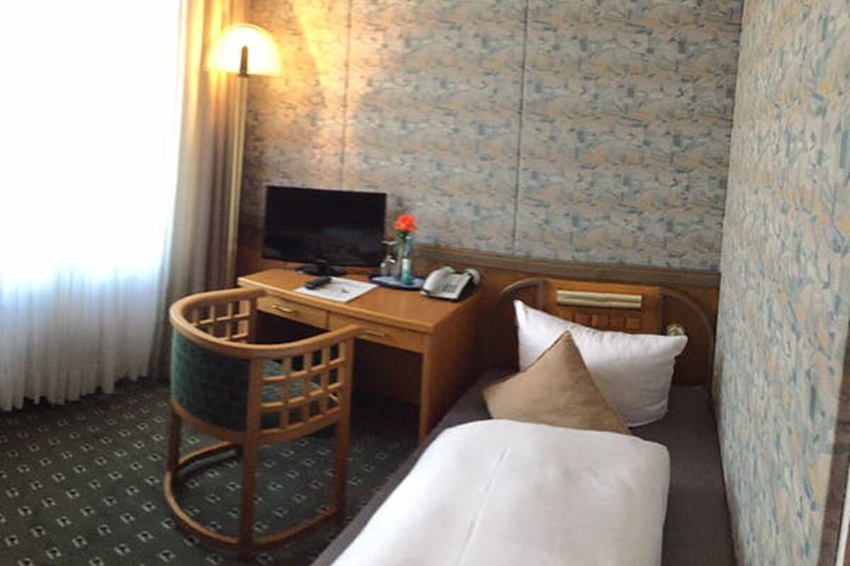 Ein Hotelzimmer mit einem Bett, einem Schreibtisch mit Computer, einem Stuhl und einer Lampe.