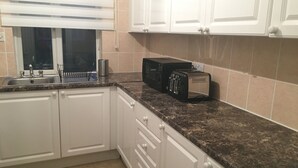 A kitchen with white cabinets, a granite countertop, a toaster, and a window with blinds. - Kingswood Apartment (London)