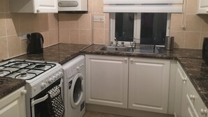 A compact kitchen with a gas stove, a built-in washing machine, a sink, and a window with blinds. - Kingswood Apartment (London)