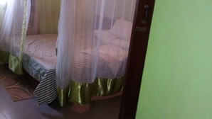 A room with a bed covered by a mosquito net, a green curtain, and a patterned bedspread. - Desai Villa Hotel (Nairobi)