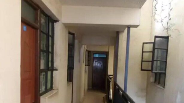 A narrow corridor with tiled flooring, a wooden door on the left, and a black railing on the right. - Desai Villa Hotel (Nairobi)