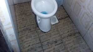 A small, basic bathroom with a toilet, a sink, and tiled walls. - Desai Villa Hotel (Nairobi)