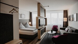 Una habitación de hotel moderna con una cama, un sofá, un televisor y una mesita.