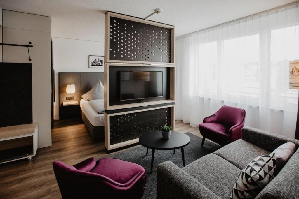 A modern living room with a flat-screen TV, a sofa, a chair, and a small table.