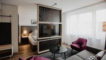 A modern living room with a flat-screen TV, a sofa, a chair, and a small table.