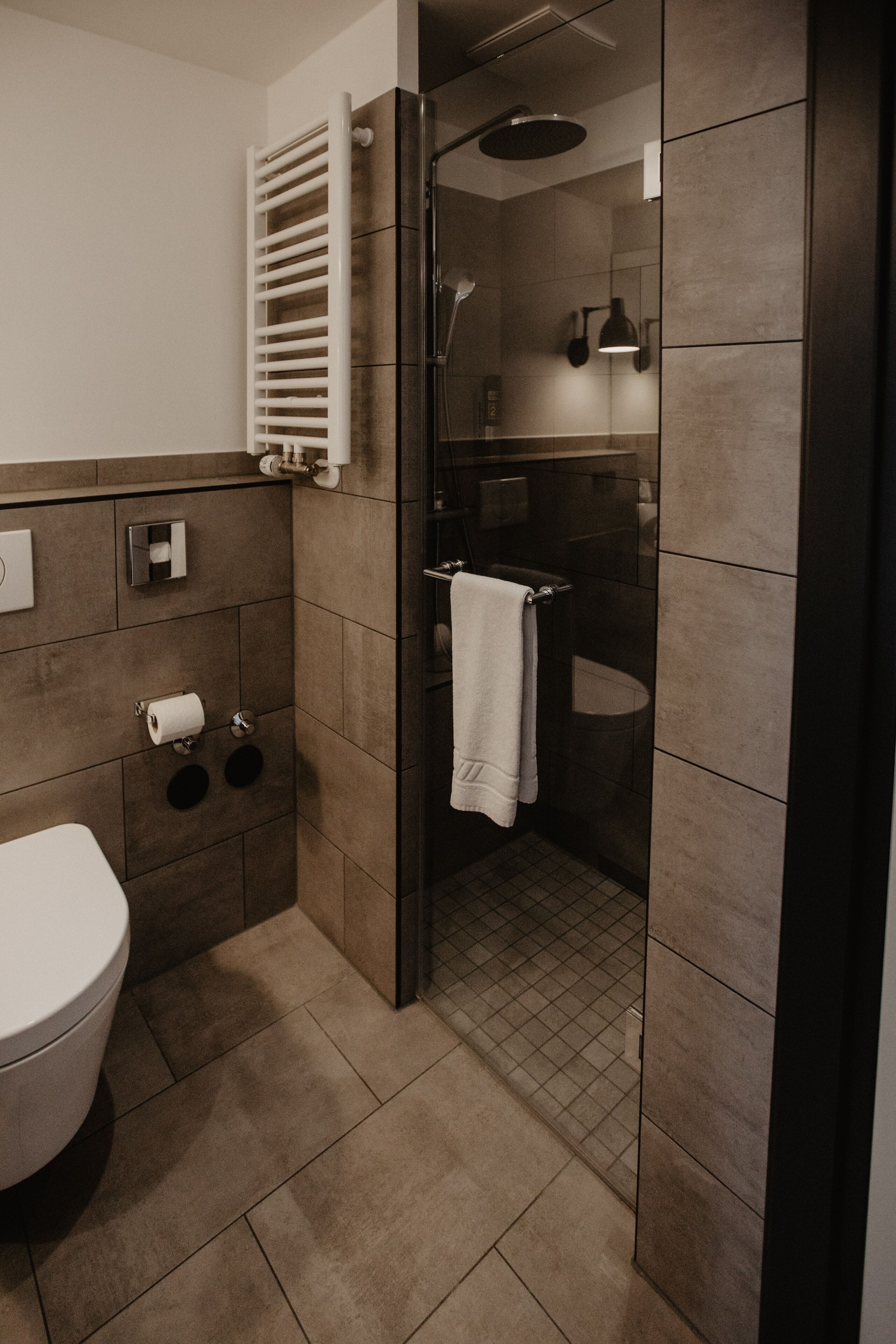 A modern bathroom with a toilet, towel rack, and a glass-enclosed shower area.