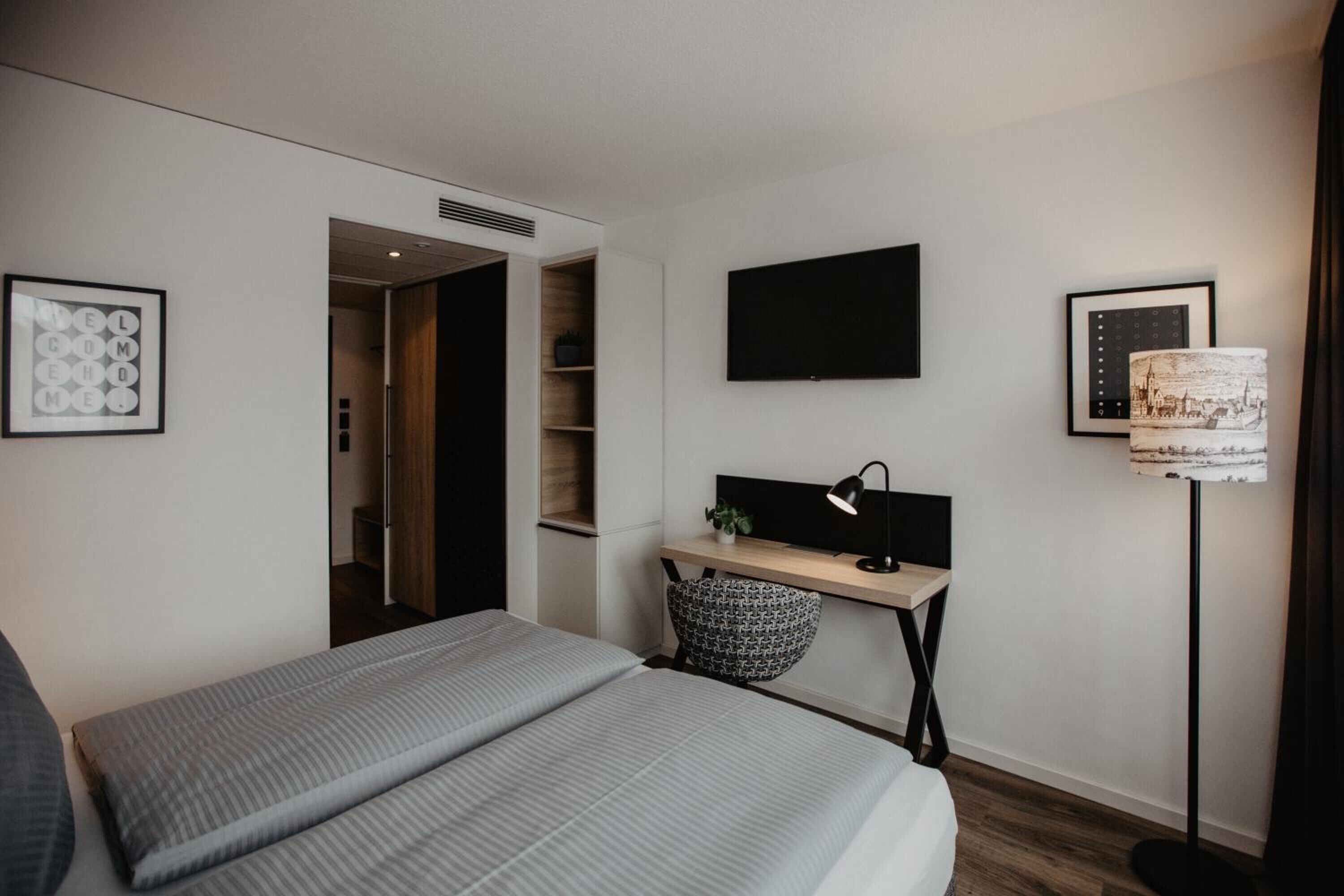 Ein modernes Schlafzimmer mit Bett, Schreibtisch, Fernseher und Lampe.