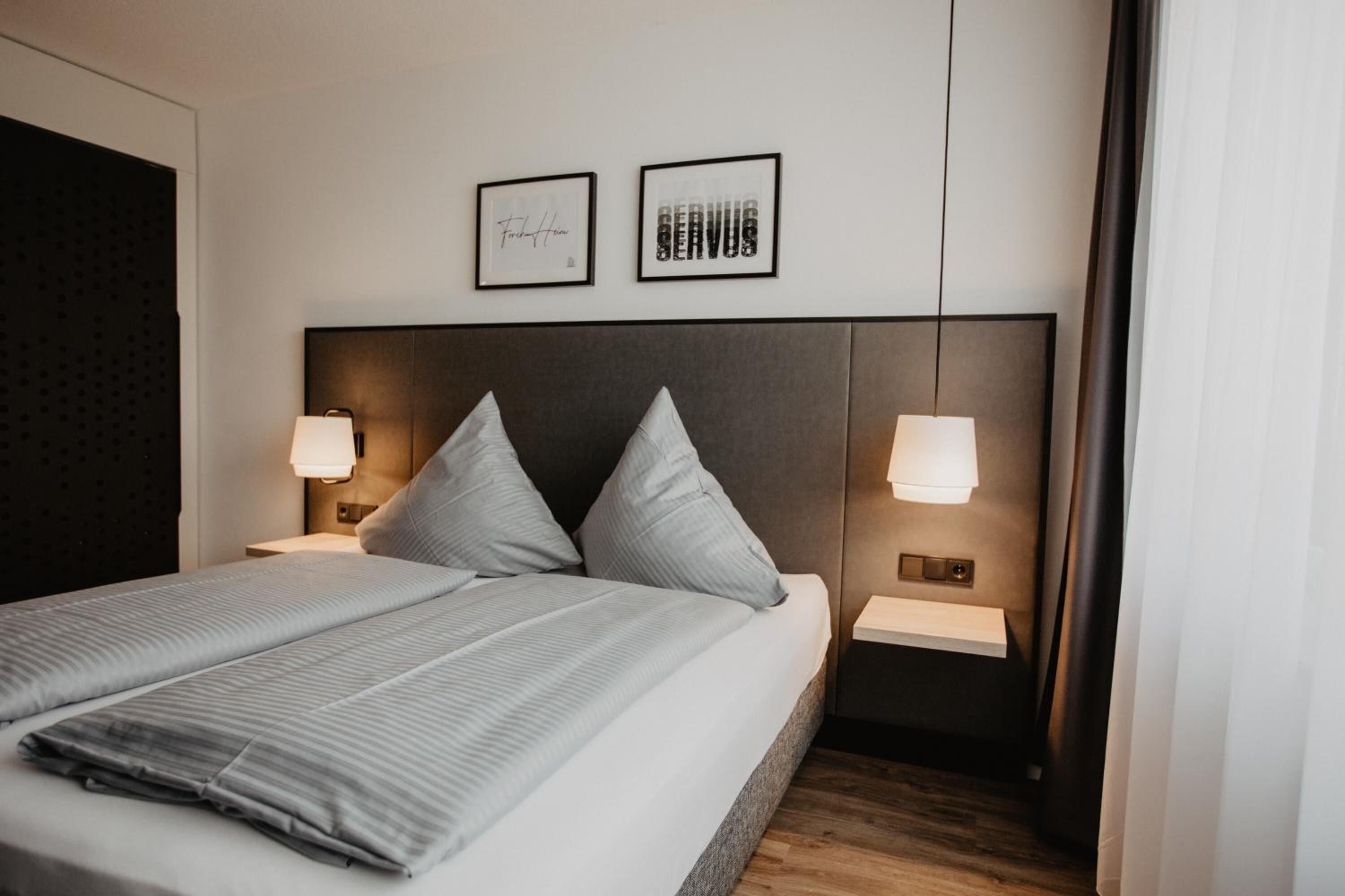 A modern hotel room with a large bed, two bedside tables, and wall-mounted lamps.