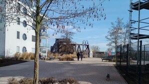 A paved walkway with a bench, a tree, and a fenced area with a metal structure. - Privatunterkunft AARON (Magdeburg)