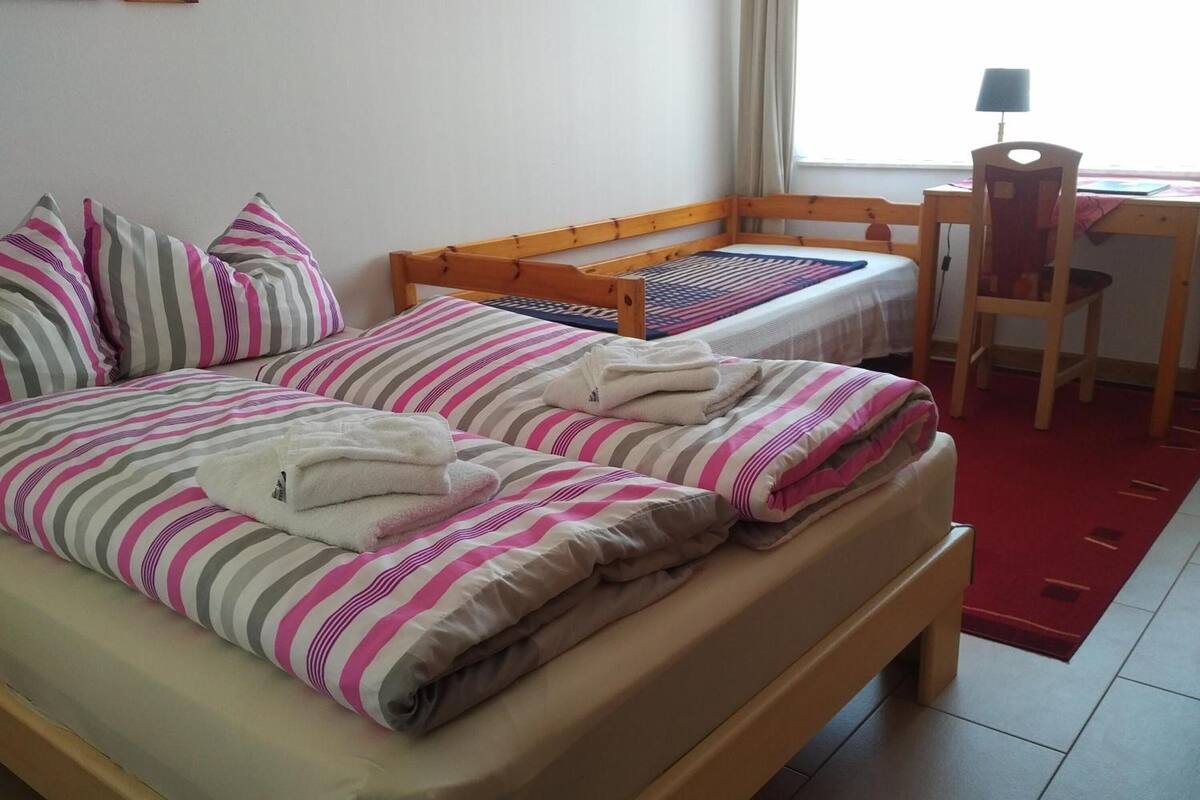 A single bed with a wooden frame, striped bedding, and a red rug.